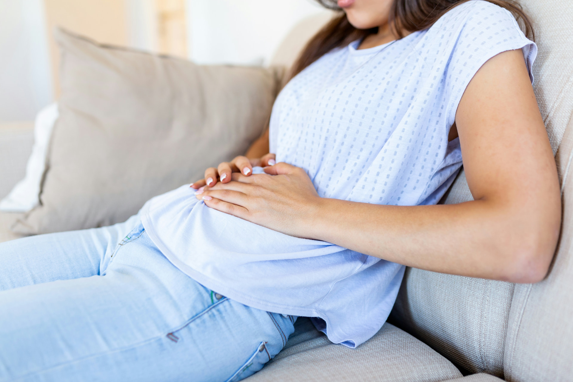 A woman sitting on a couch holds her abdomen with both hands