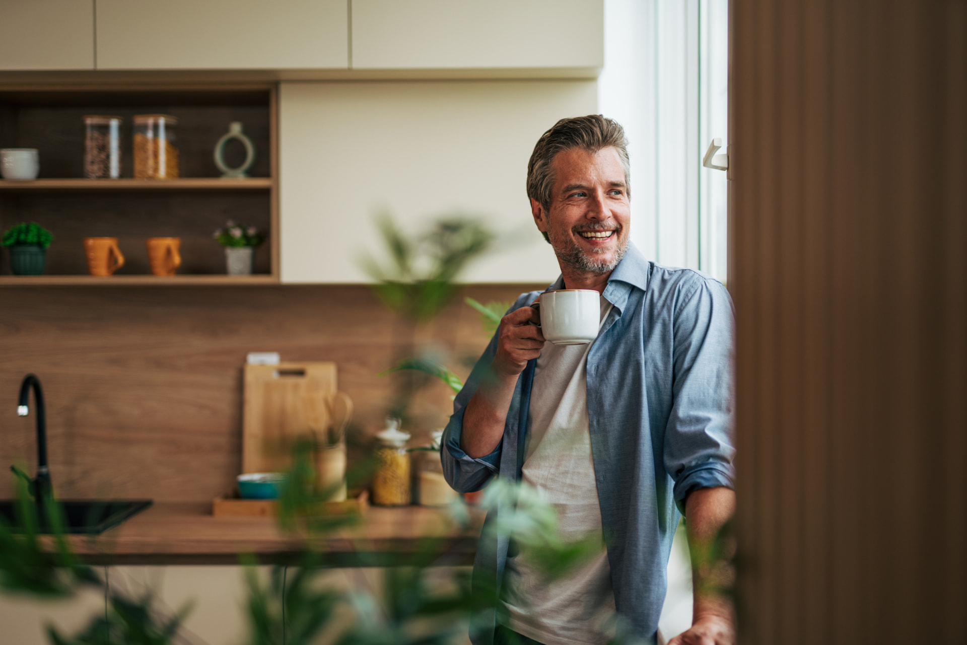 Smiling mature man drinking coffee in his kitchen and looking out the window