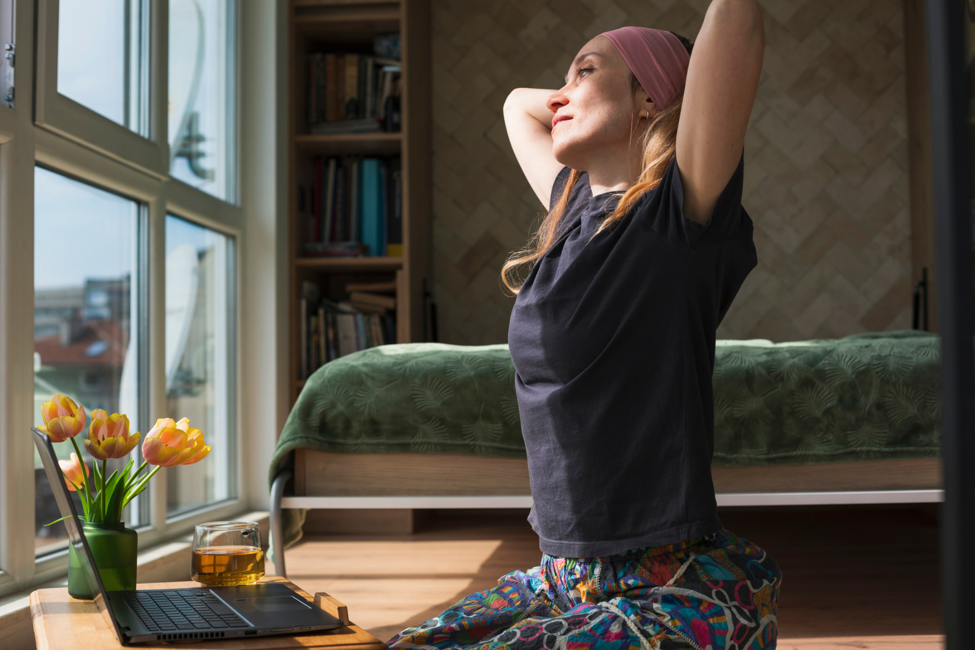 Woman stretching at her desk beside a sunlit window during a work break