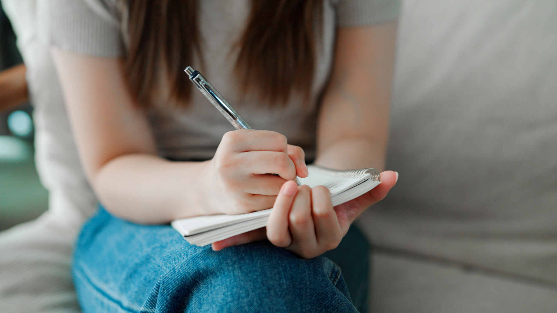Woman sitting on a couch writing notes in a small notebook