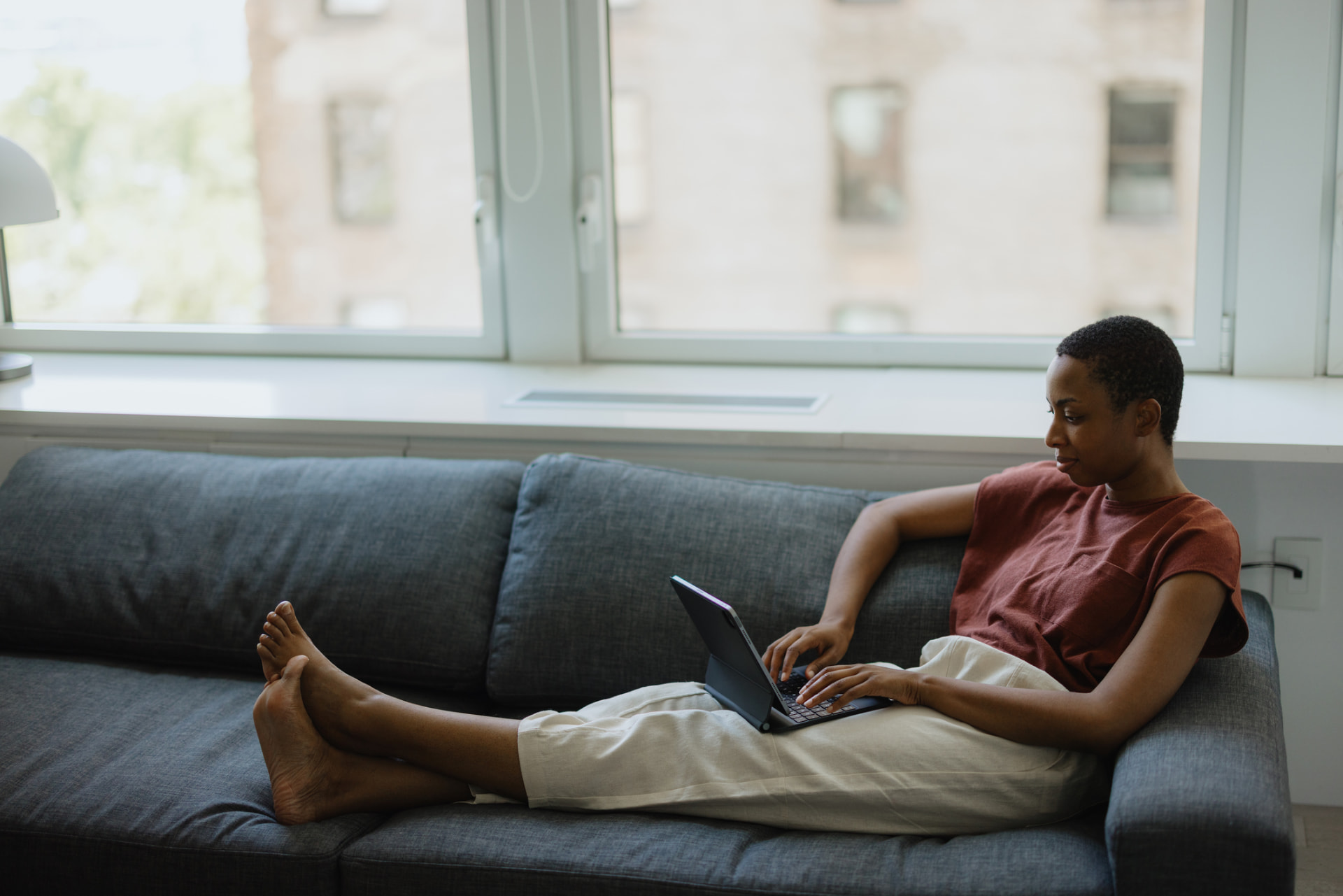 A woman relaxed on her sofa at home joining a telehealth follow-up visit on her laptop