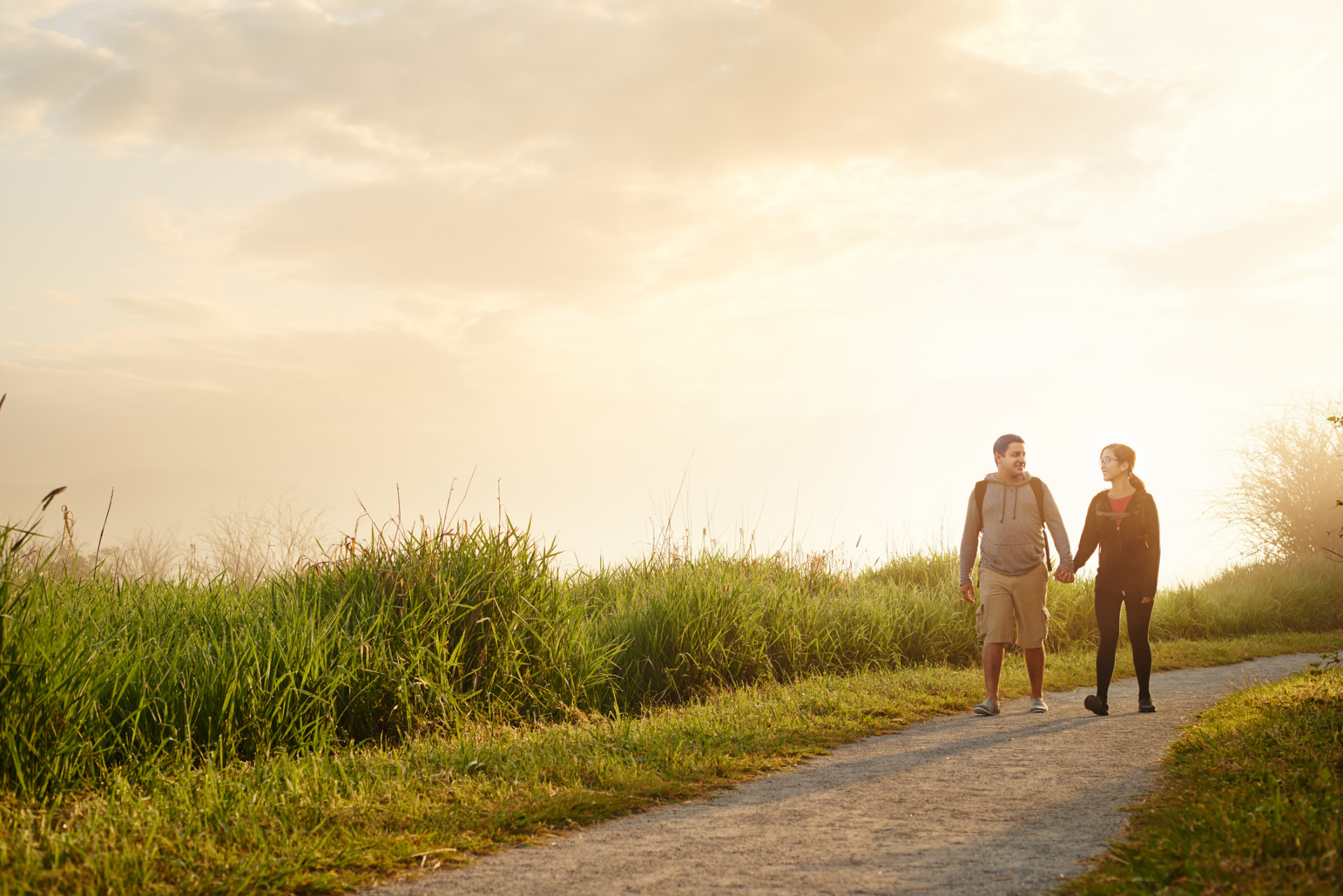 Couple walking together on a grassy trail at sunrise