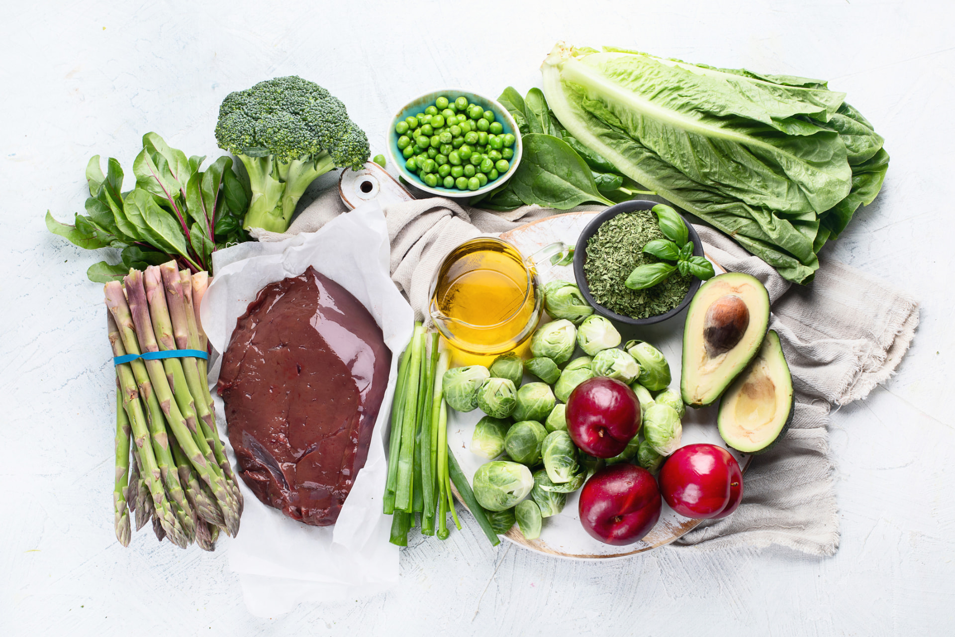 Overhead spread of fresh low-histamine foods — greens, asparagus, avocado, olive oil, and fresh meat
