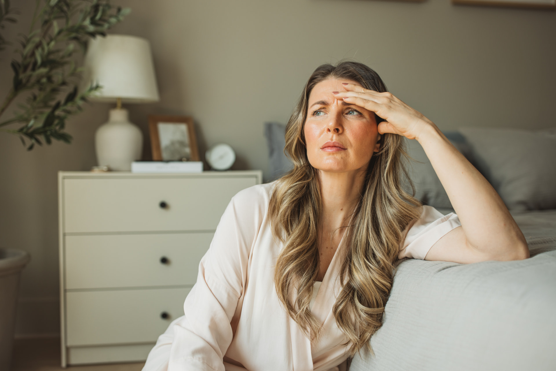 A woman sitting on the edge of her bed in the morning, tired after a poor night of sleep