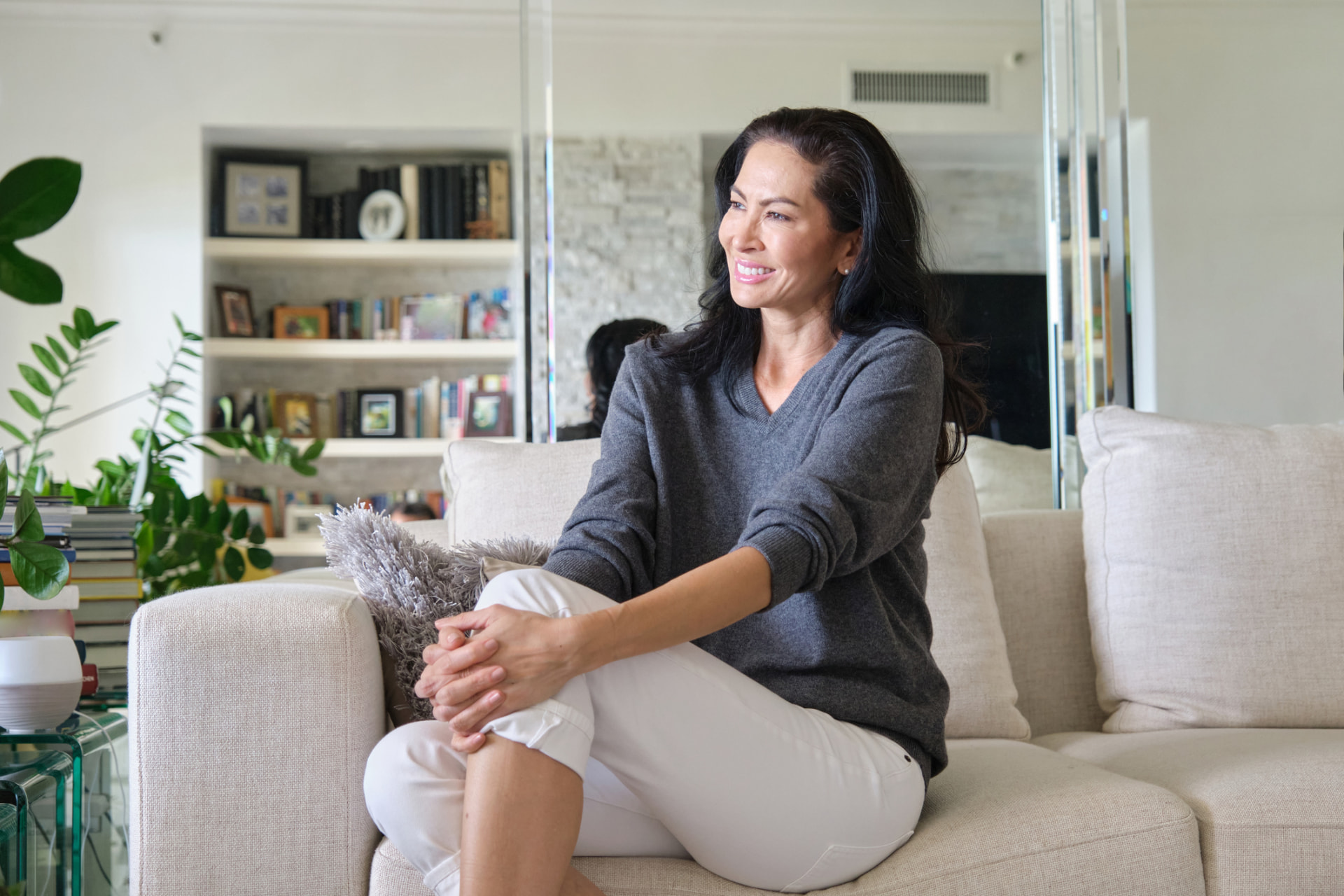 A woman in a grey sweater sitting relaxed on a light-colored couch