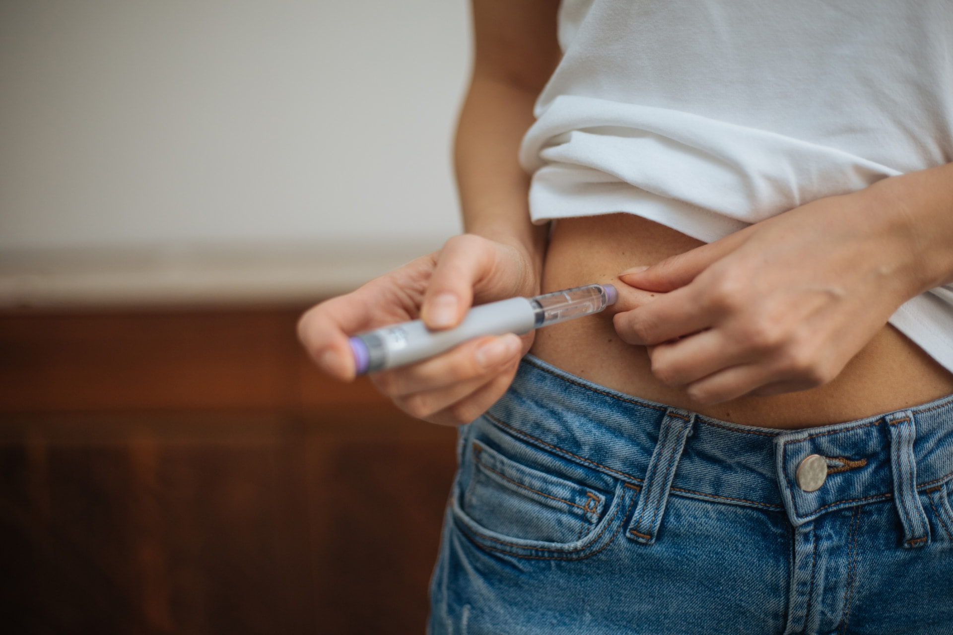 Person administering a GLP-1 injection pen into the abdomen at home