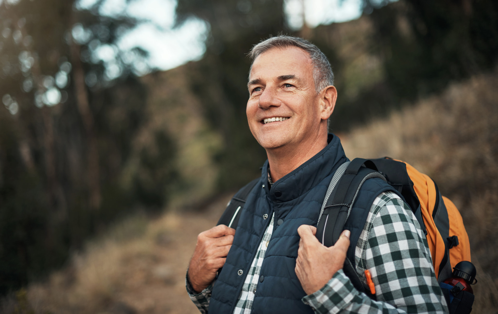 Man in his sixties hiking a wooded trail with a backpack, looking ahead