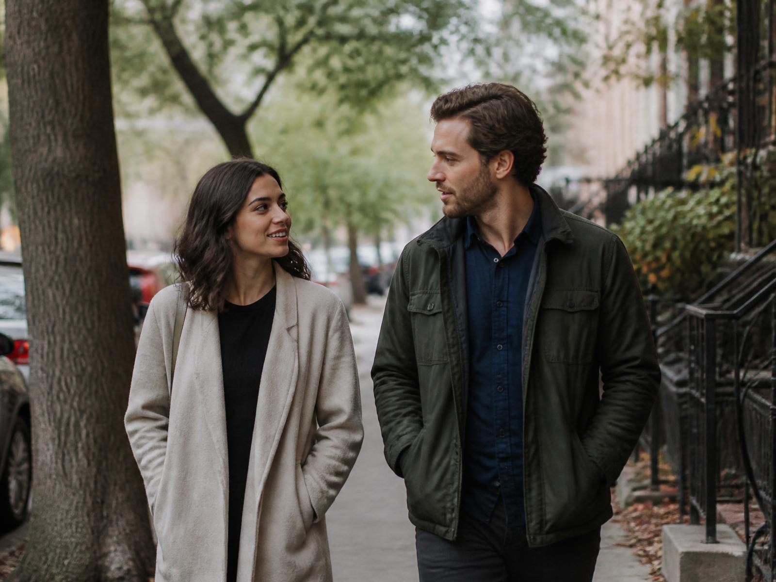 A couple walking and talking together on a tree-lined city sidewalk