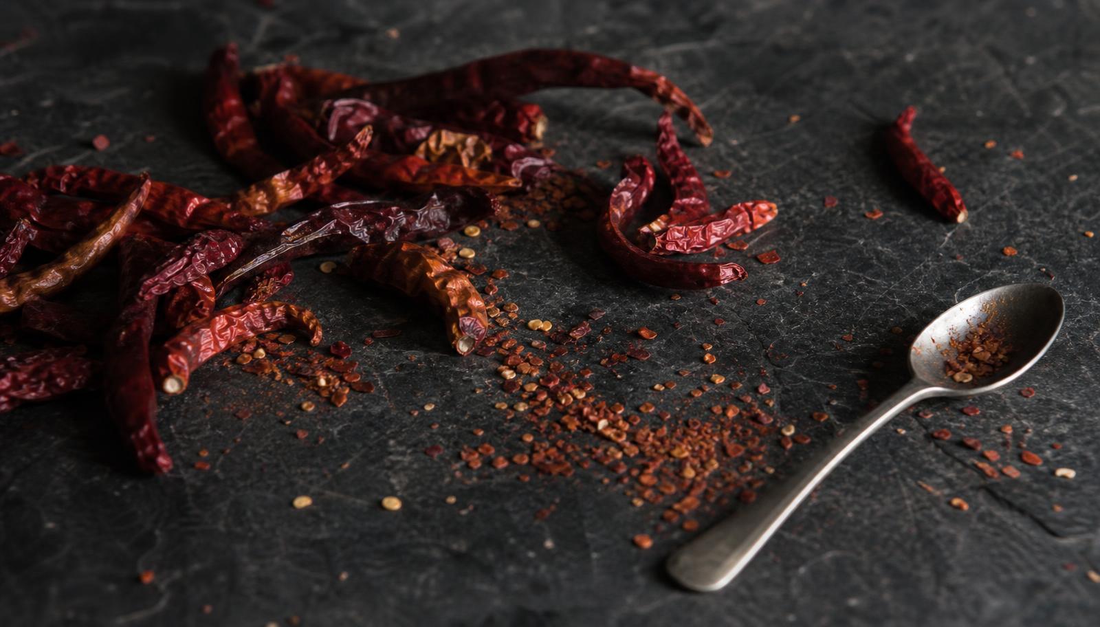 Dried red chili peppers, peppercorns, star anise and cinnamon on a dark slate surface