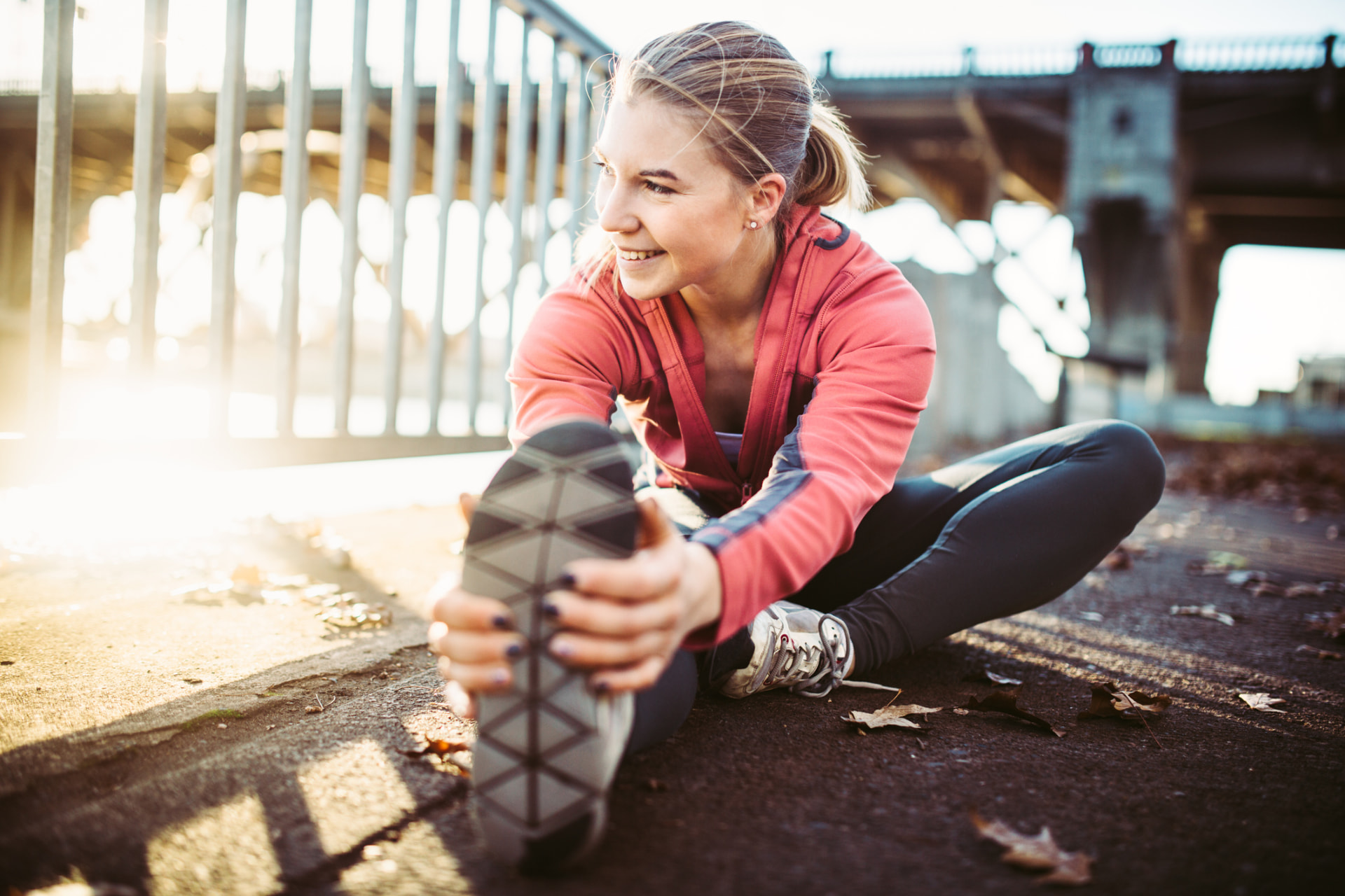A woman stretching outdoors on a riverfront path in warm morning sunlight